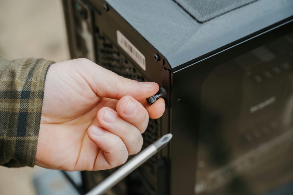 Close-up of a hand unscrewing a desktop computer case, emphasizing technology maintenance.