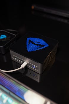 Compact mini PC with customizable digital display glowing in blue on a dark desk setup.