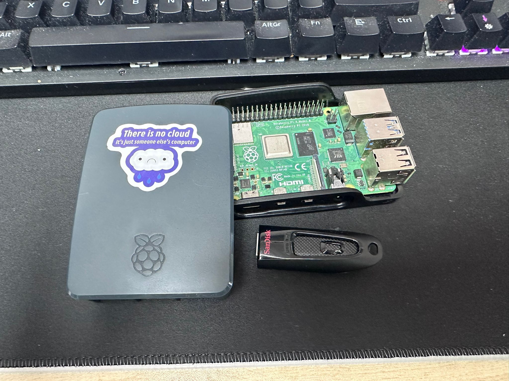 Raspberry Pi 4 board next to its case showing the There is no cloud sticker, with a SanDisk USB drive alongside
